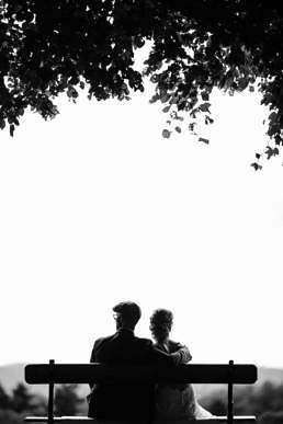 couple sitting on bench under tree grayscale photography