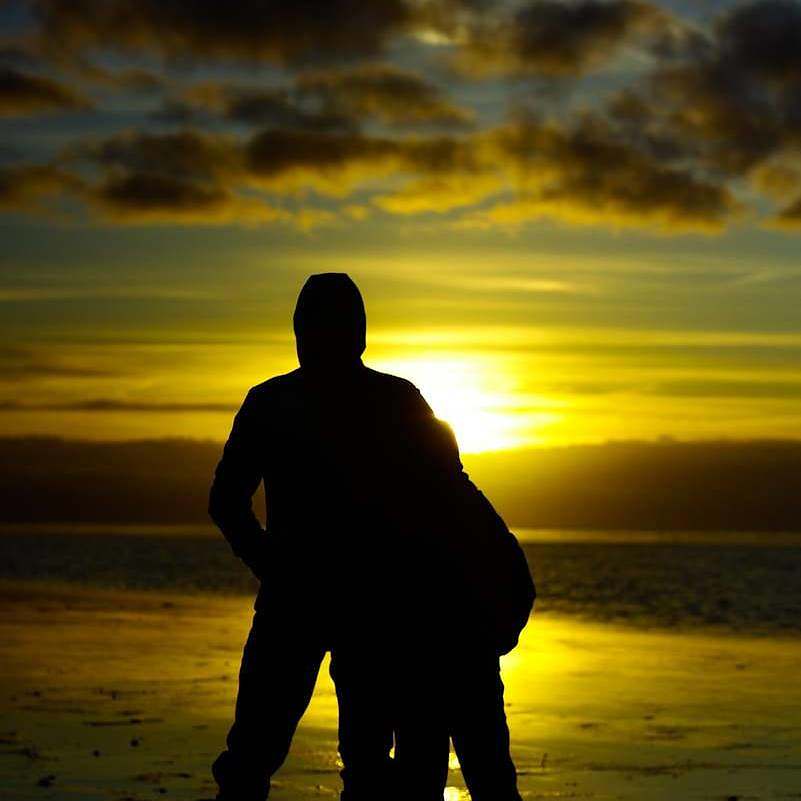 silhouette photo of two persons standing beside beach
